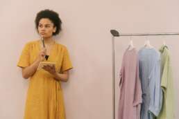 a thinking woman standing besides clothes hanging on cloth hanger