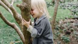 child smiling in nature holding a tree